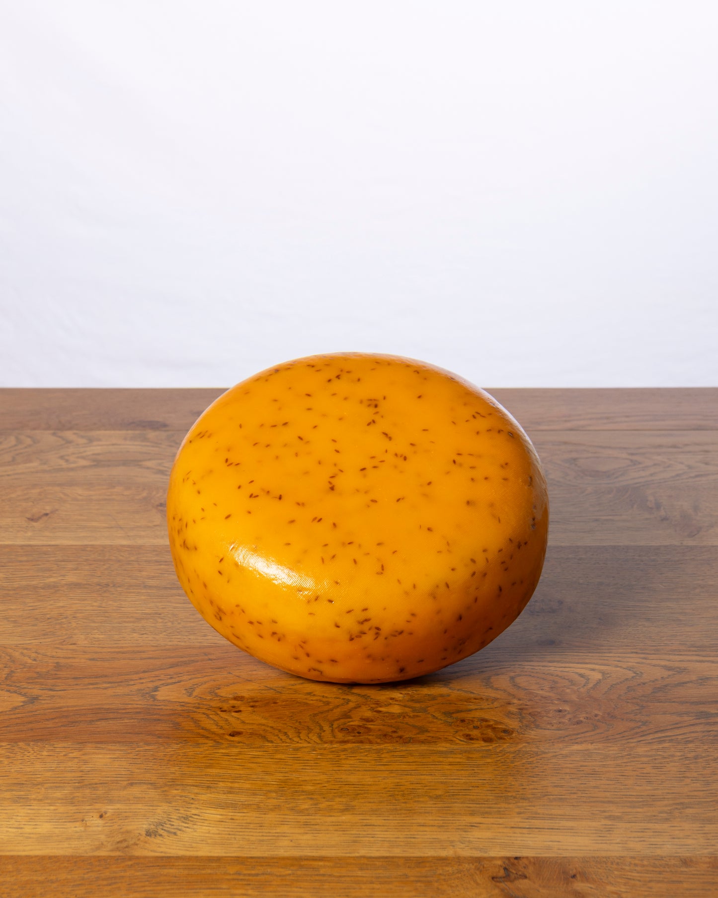 Een hele Komijn 48+ Jong kaaswiel op een houten tafel.