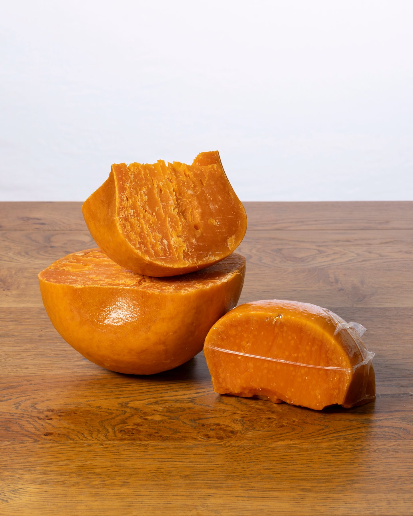 Een balvormige Commissie 40+ Extra Oud kaas, in drie stukken gesneden, waarbij elk stuk vacuümverpakt is in plastic.