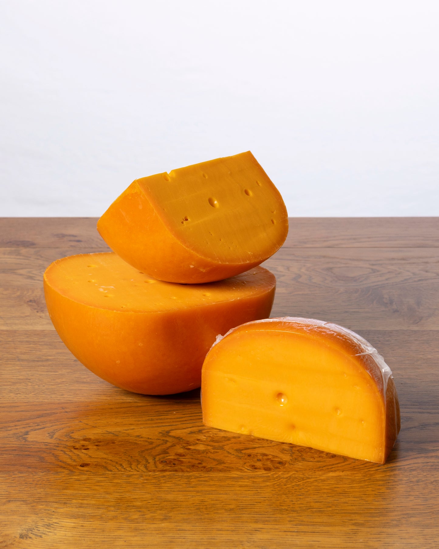 Een balvormige Commissie 40+ Jong Belegen kaas, in drie stukken gesneden, waarbij elk stuk vacuümverpakt is in plastic.