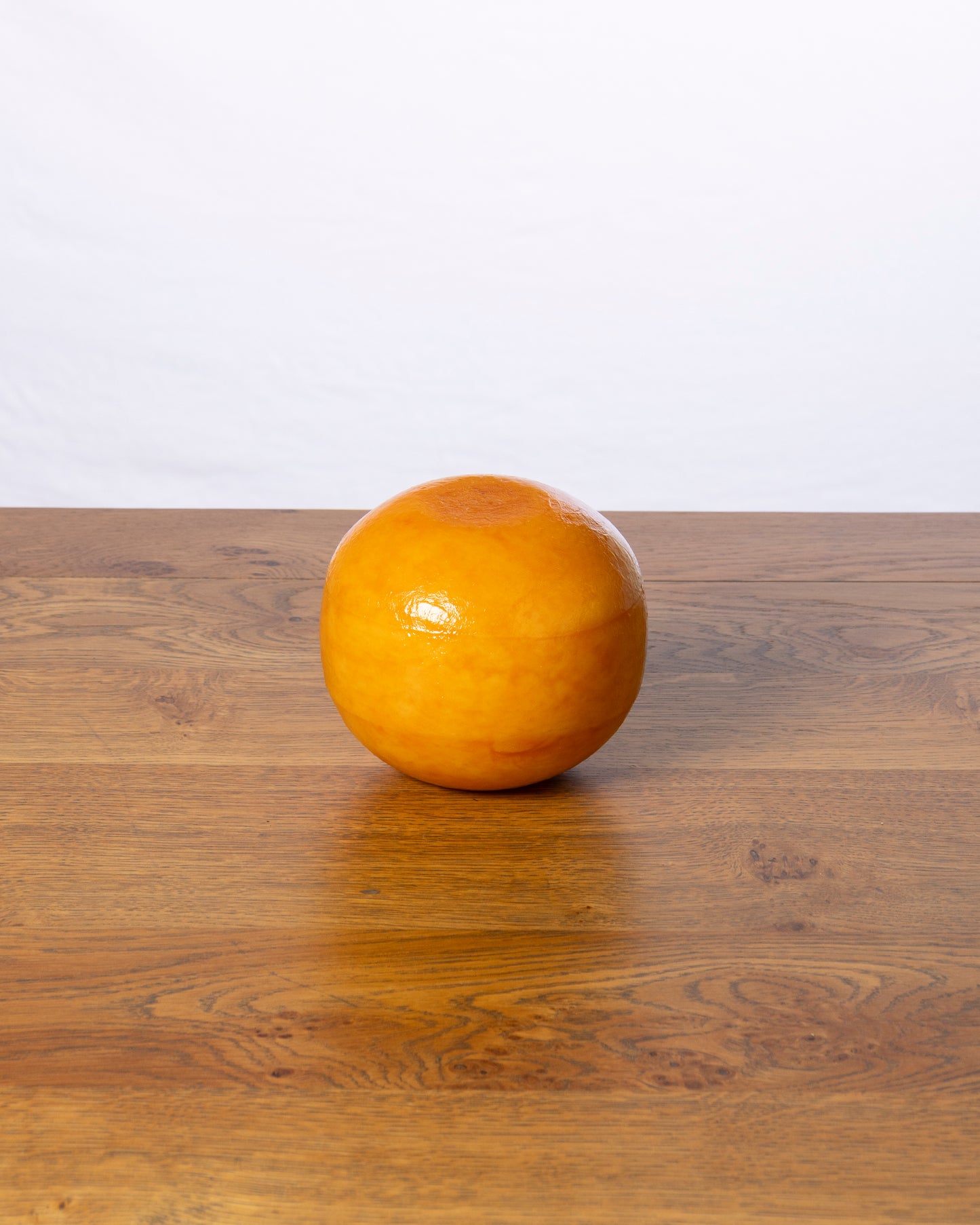 Een hele bolvormige Edammer 40+ Belegen op een houten tafel.