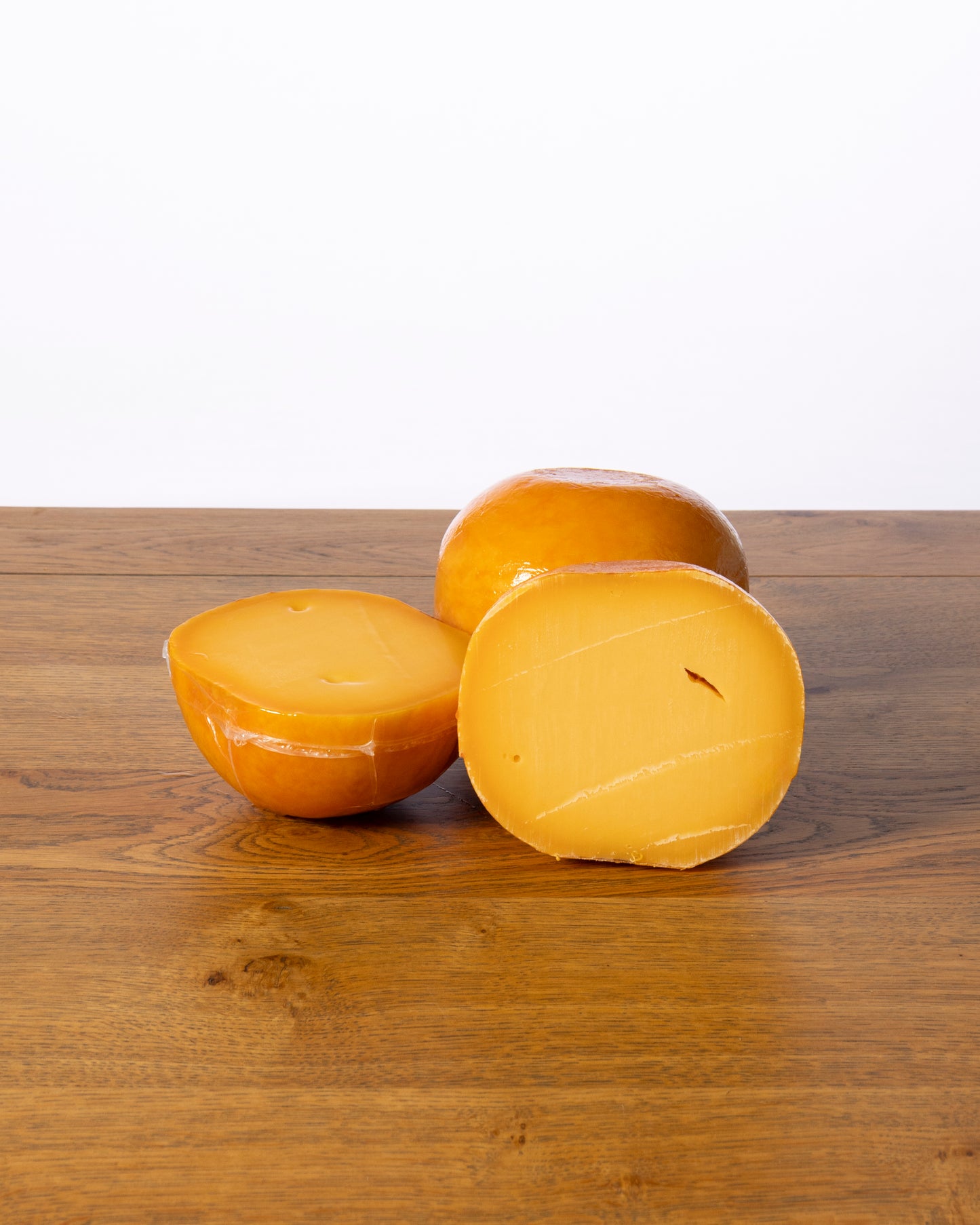 Een bolvormige Edammer 40+ Belegen, in drie stukken gesneden, waarbij elk stuk vacuümverpakt is in plastic.