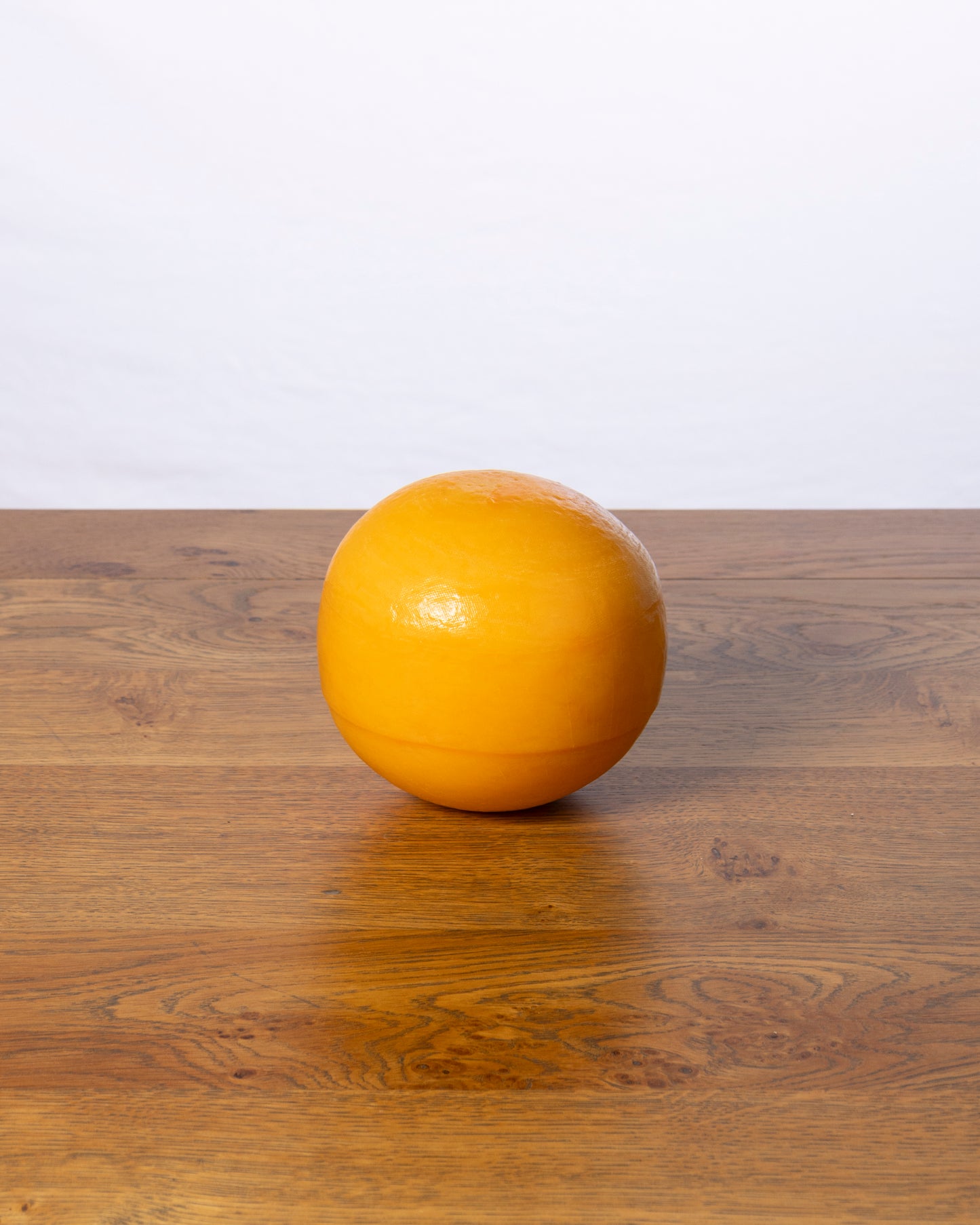 Een hele bolvormige Edammer 40+ Jong Belegen op een houten tafel.