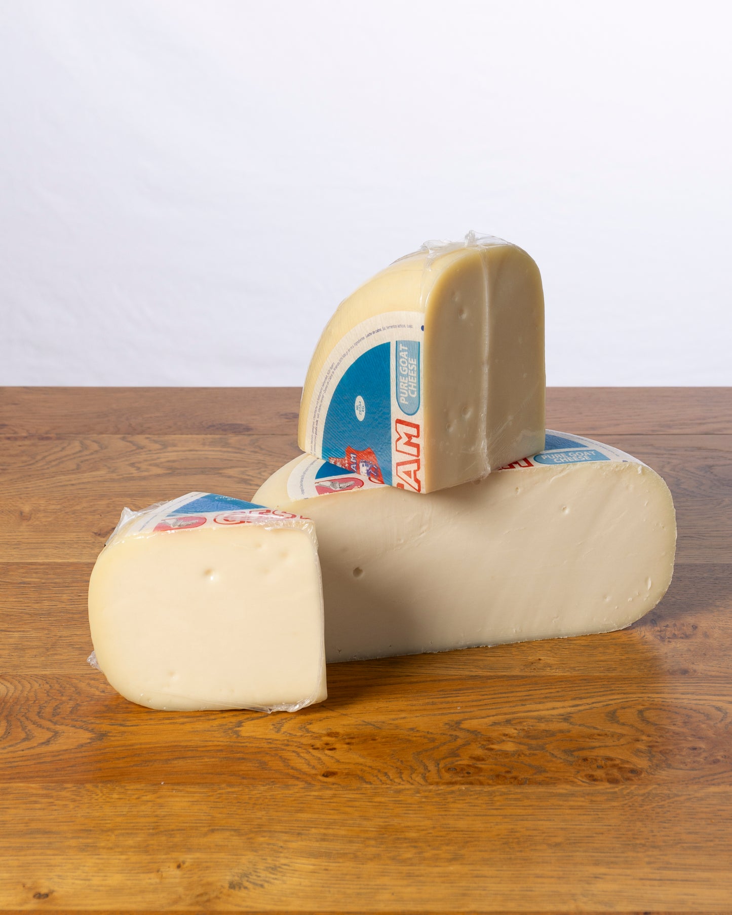 Een wielvormige Geitenkaas 50+ Jong, in drie stukken gesneden, waarbij elk stuk vacuümverpakt is in plastic.