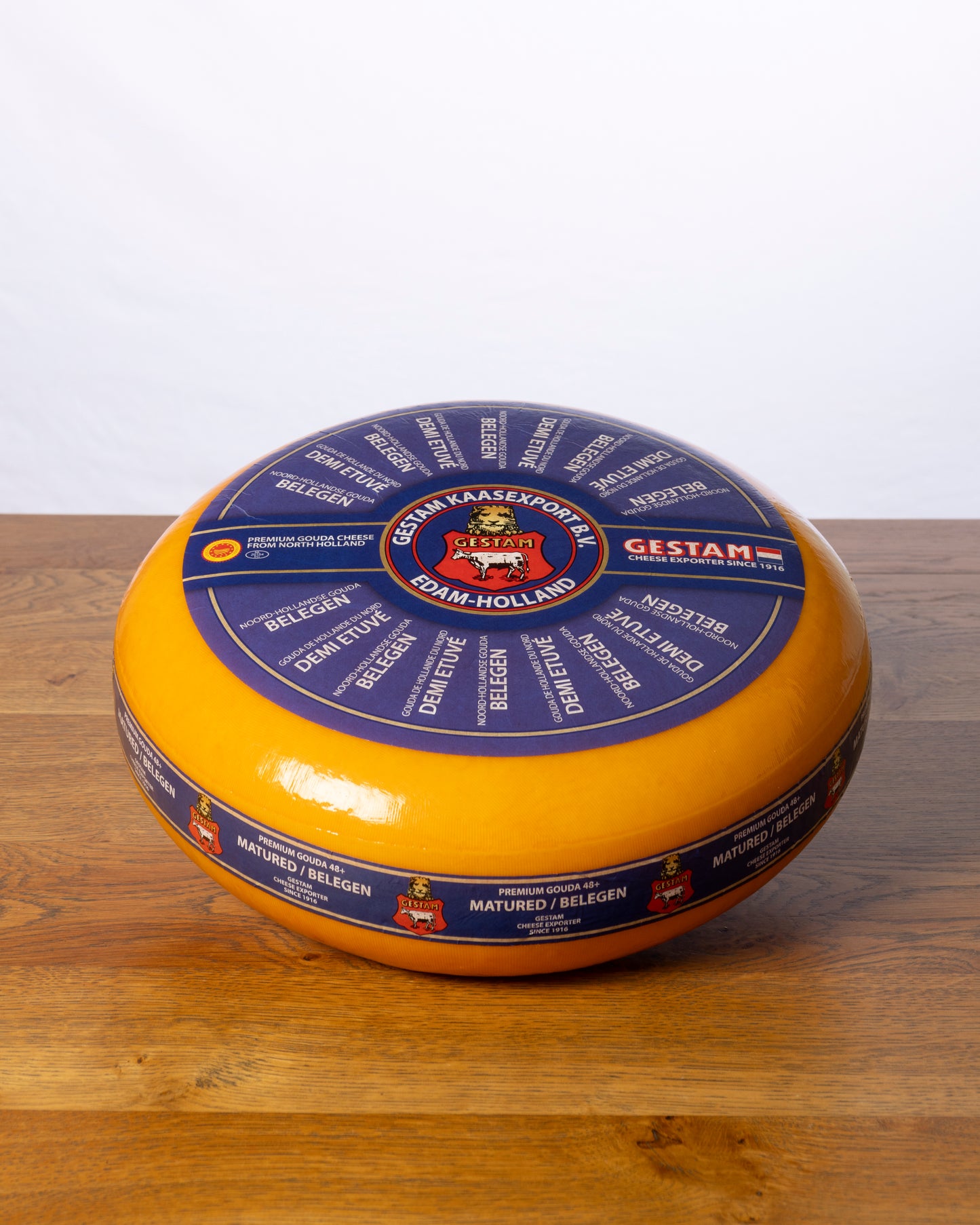 Een hele wielvormige Goudse 48+ Belegen op een houten tafel.