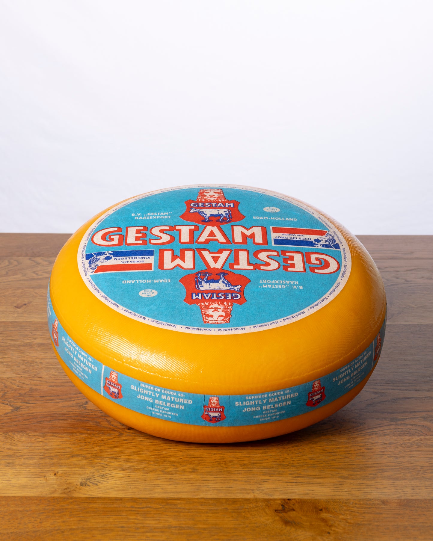 Een hele wielvormige Goudse 48+ Jong Belegen op een houten tafel.