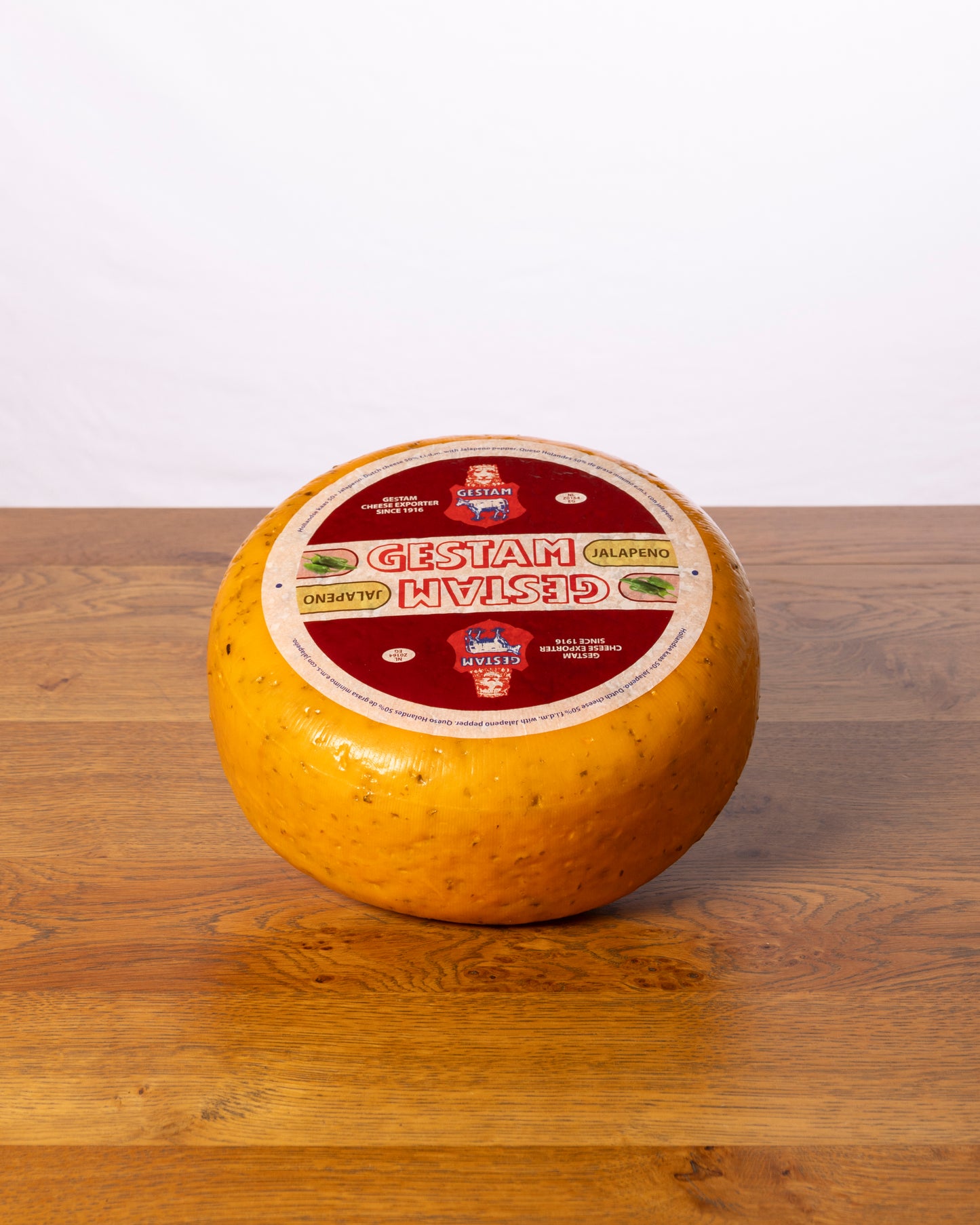 Een hele wielvormige Jalapeño 50+ Jong kaas op een houten tafel.
