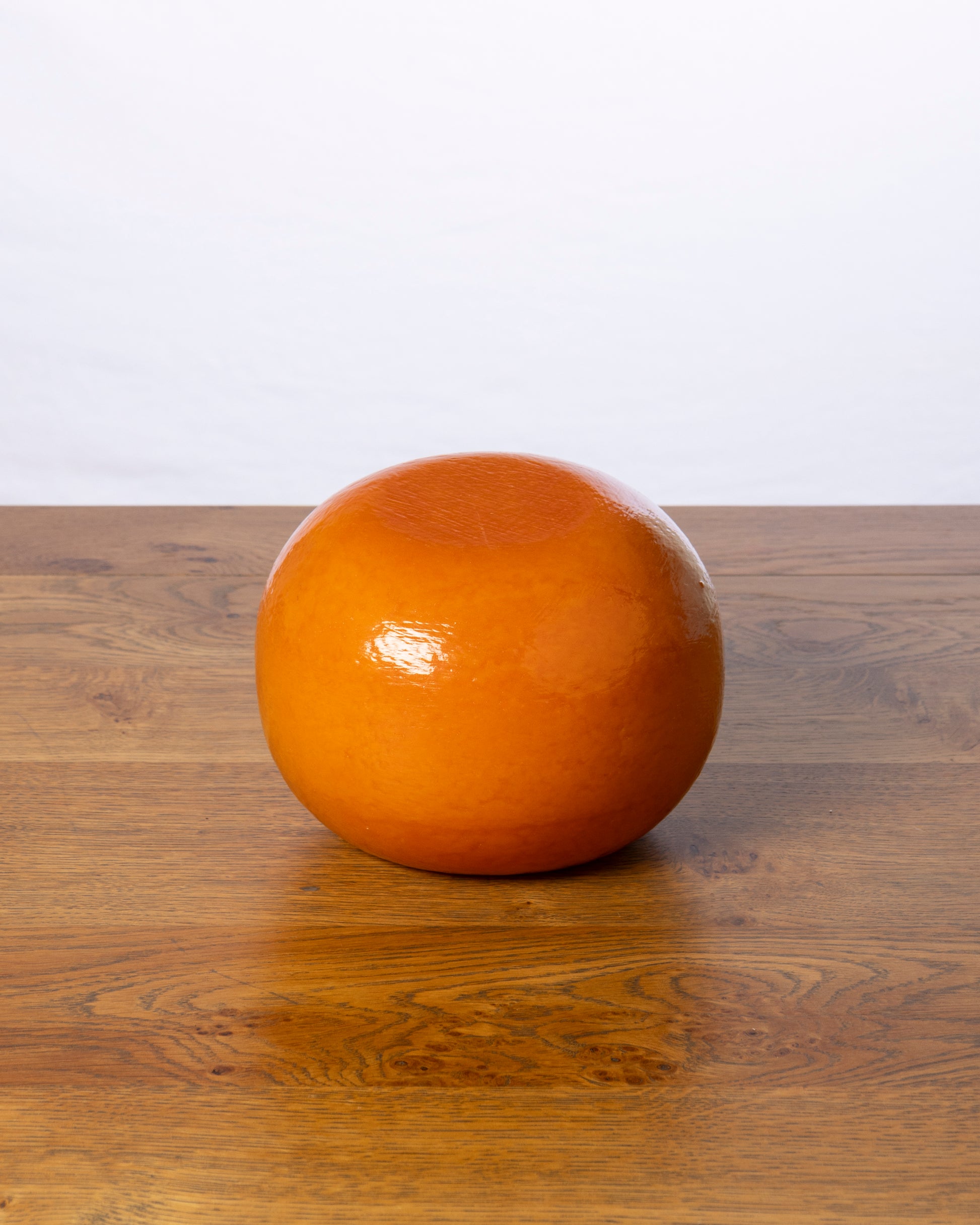 Een hele balvormige Commissie 40+ Belegen kaas op een houten tafel.